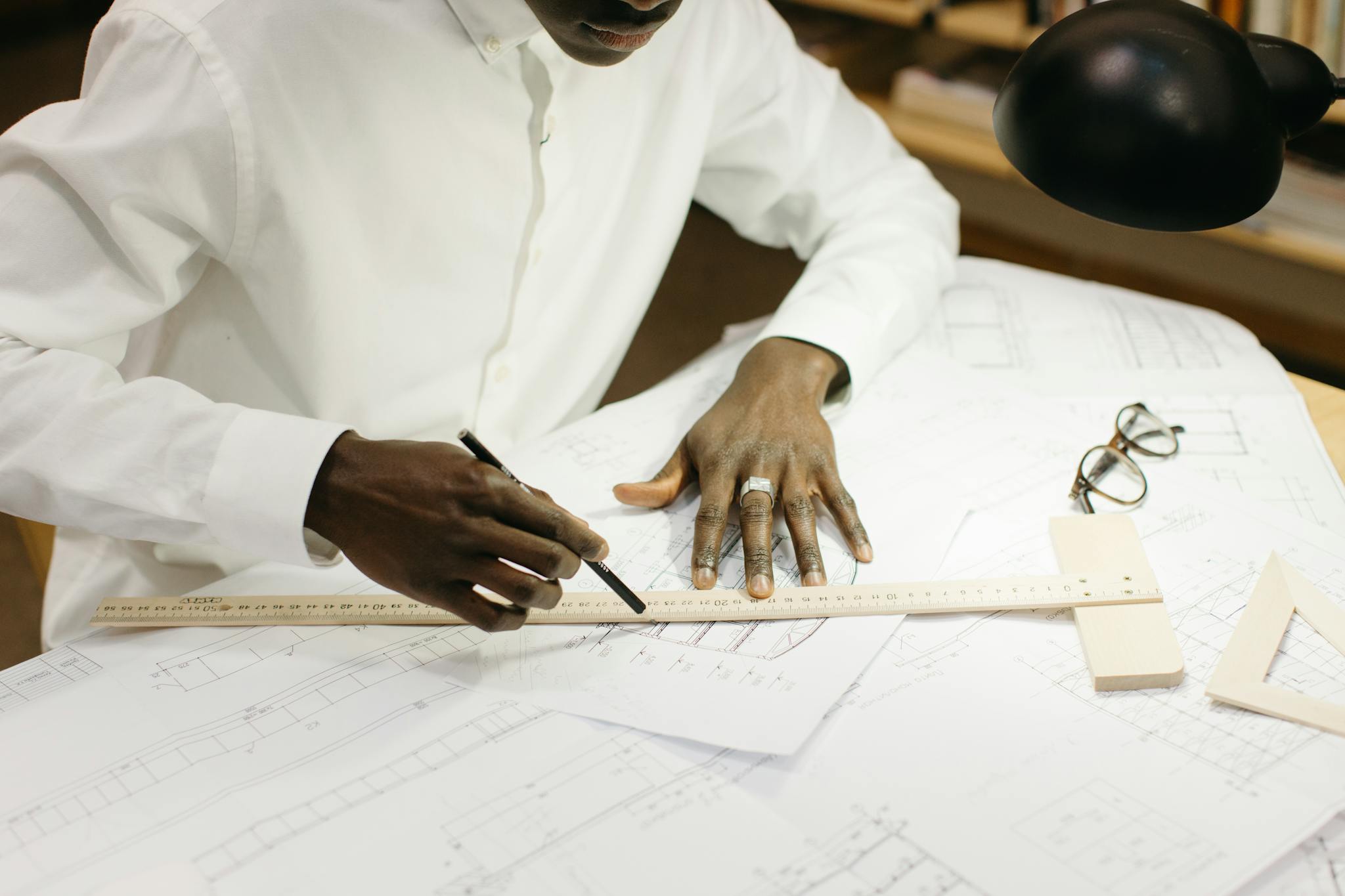 An architect diligently works on blueprints at a well-lit office desk with design tools.