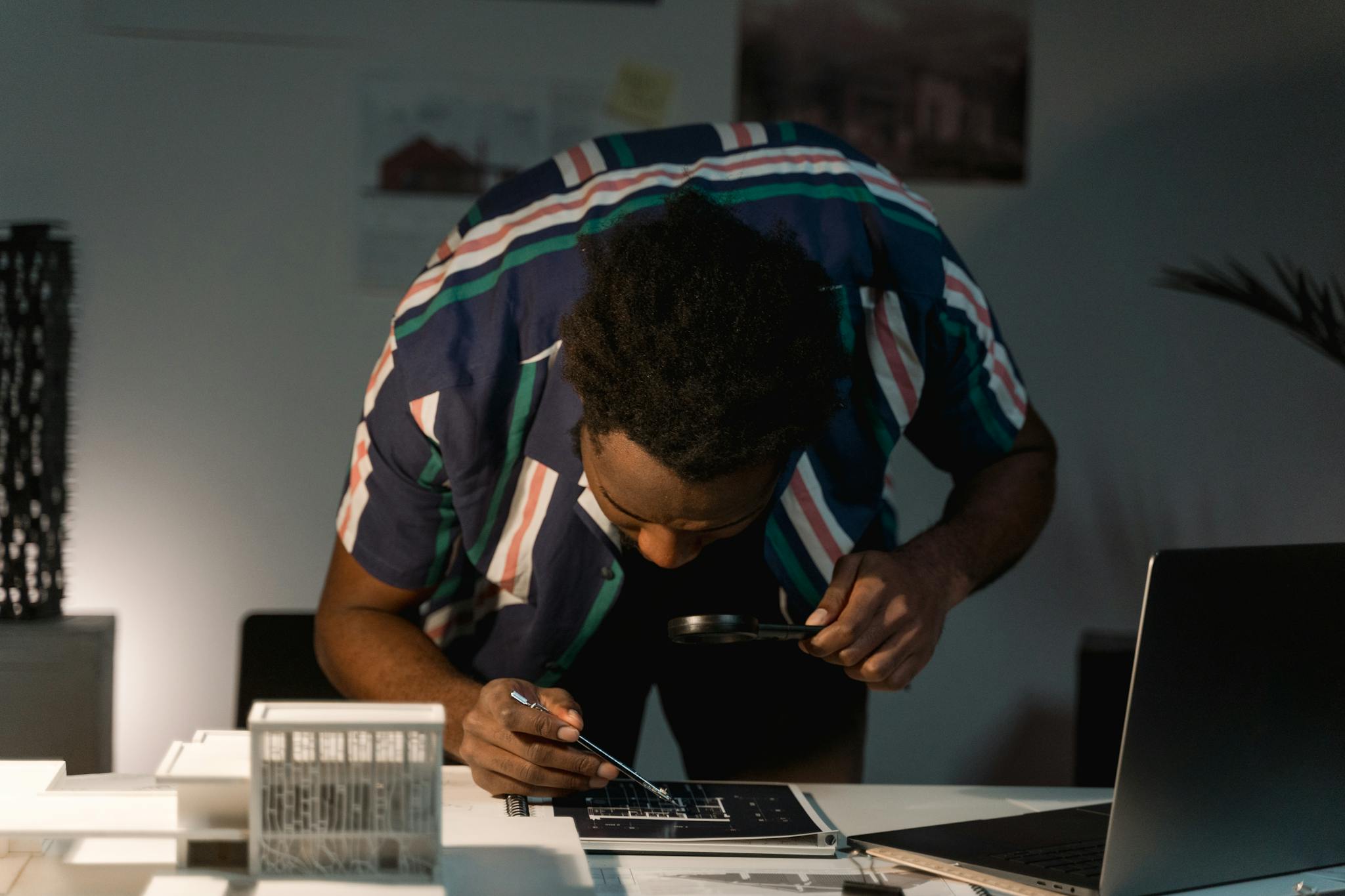 Architect examining blueprints with a magnifying glass in a modern office environment.