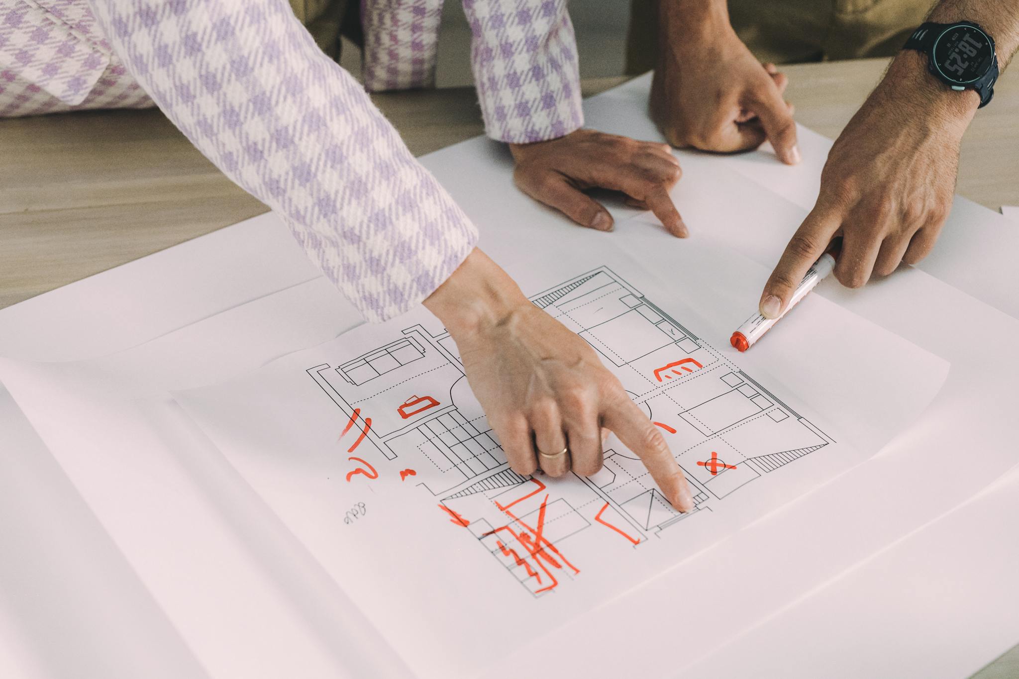 Hands pointing and discussing a floor plan in a collaborative workspace setting.