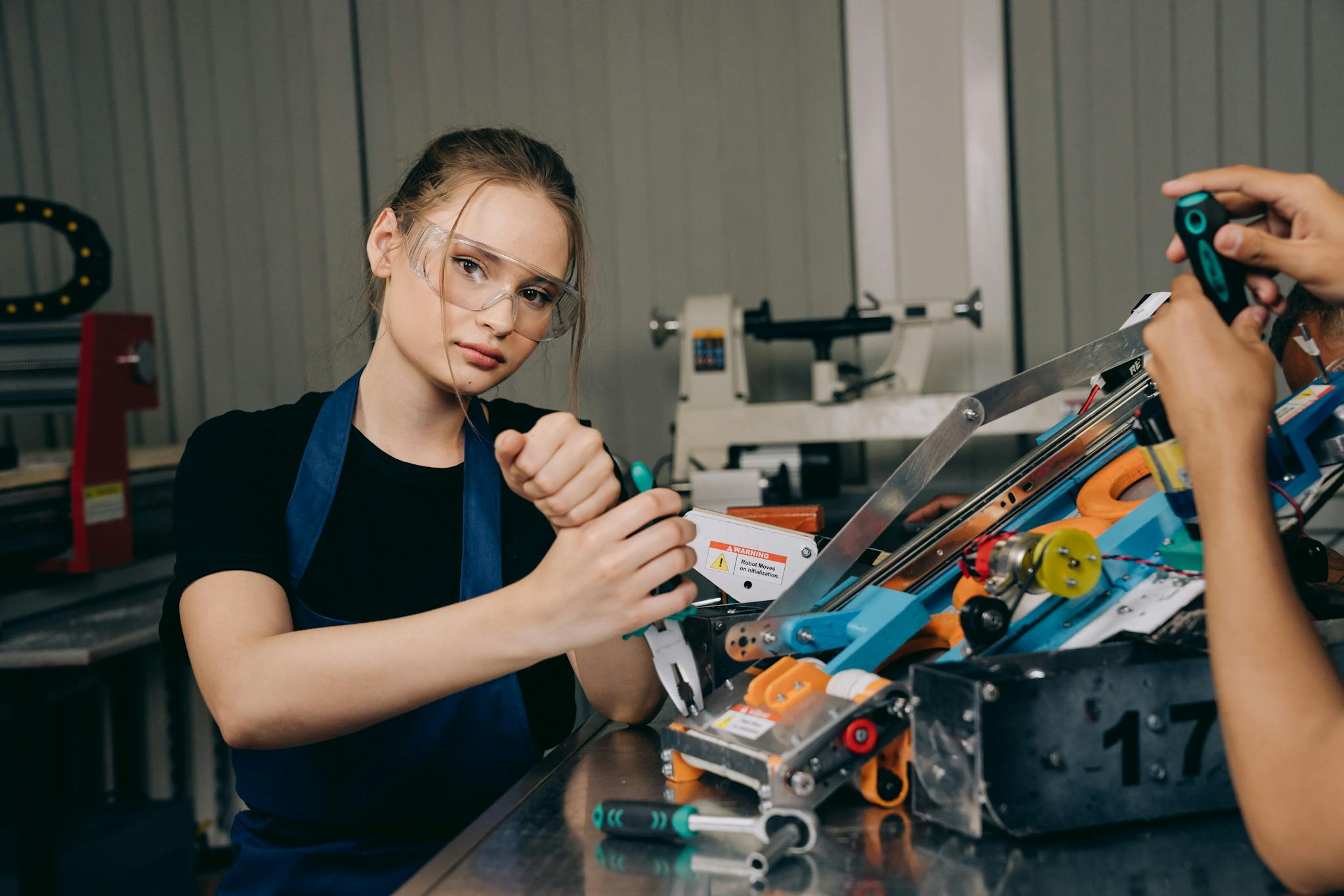 Young woman in a workshop assembling robotic components wearing protective goggles.